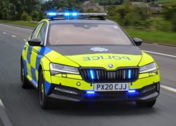 Police car driving on a road with blue lights on, marked with police and a license plate reading PX20 CJJ.