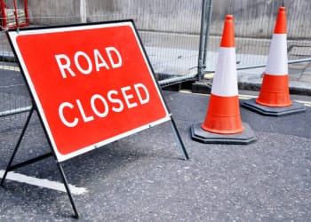 A road closed sign accompanied by two orange and yellow traffic cones