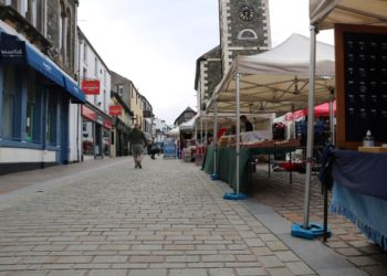 Keswick Market with the stalls on the right and shops on the left. The clock tower is in the background