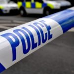 A generic picture of police tape running across a road and police cars are in the background