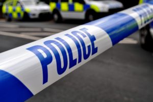 A generic picture of police tape running across a road and police cars are in the background