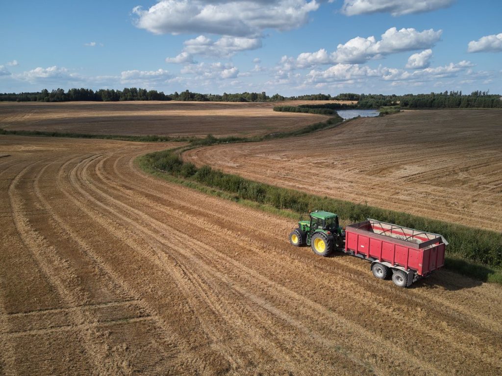A tractor on farmland with blue skies above and clouds