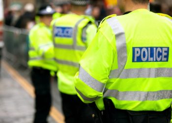 Three police officers stand chatting with their backs to the camera. The back of one officer is in focus while the other two are blurred