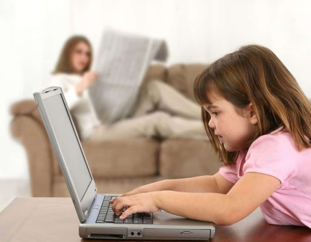 Child with laptop wihile woman reads newspaper in background