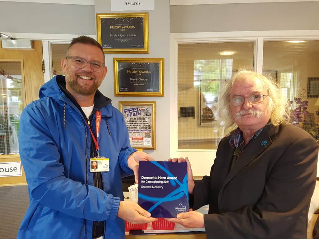 John Kemp from Alzheimer's Society presenting organiser Graeme McGrory with Dementia Hero Award For Campaigning at Dalton Court on June 25, when a gig was due to take place there