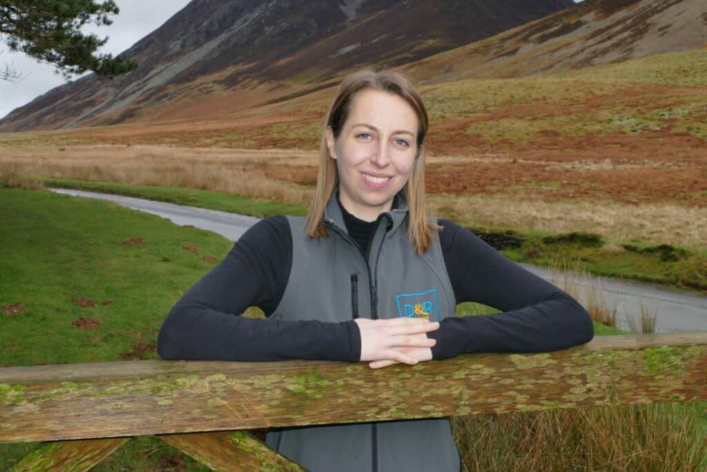 Davidson & Robertson (D&R) have appointed Abigail Wass as Assistant Land Agent. She is pictured in the countryside with her hands resting on a fence with farmland in the background. She is wearing a sleeveless D&R jacket and a black long-sleeved top underneath. She has shoulder-length blonde hair and is smiling
