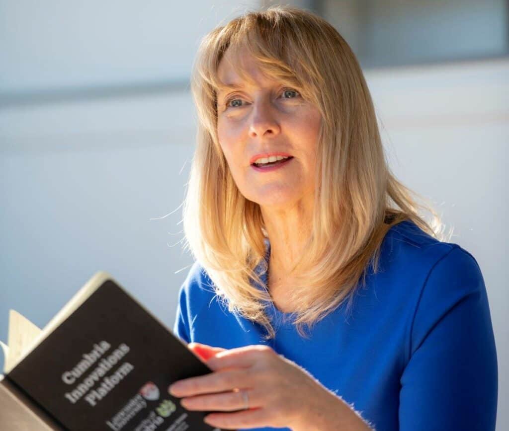 CUSP II lead Sarah Allison holds a book as she speaks. She is wearing a blue blouse and has blonde hair