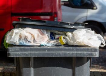 A grey wheelie bin overflowing with rubbish