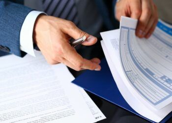man flicking through paperwork with a pen in his hand