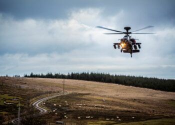 A helicopter flies in RAF Spadeadam with greys skies behind it