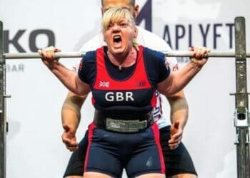 Sharon Holmes powerlifting with her trainer behind her.