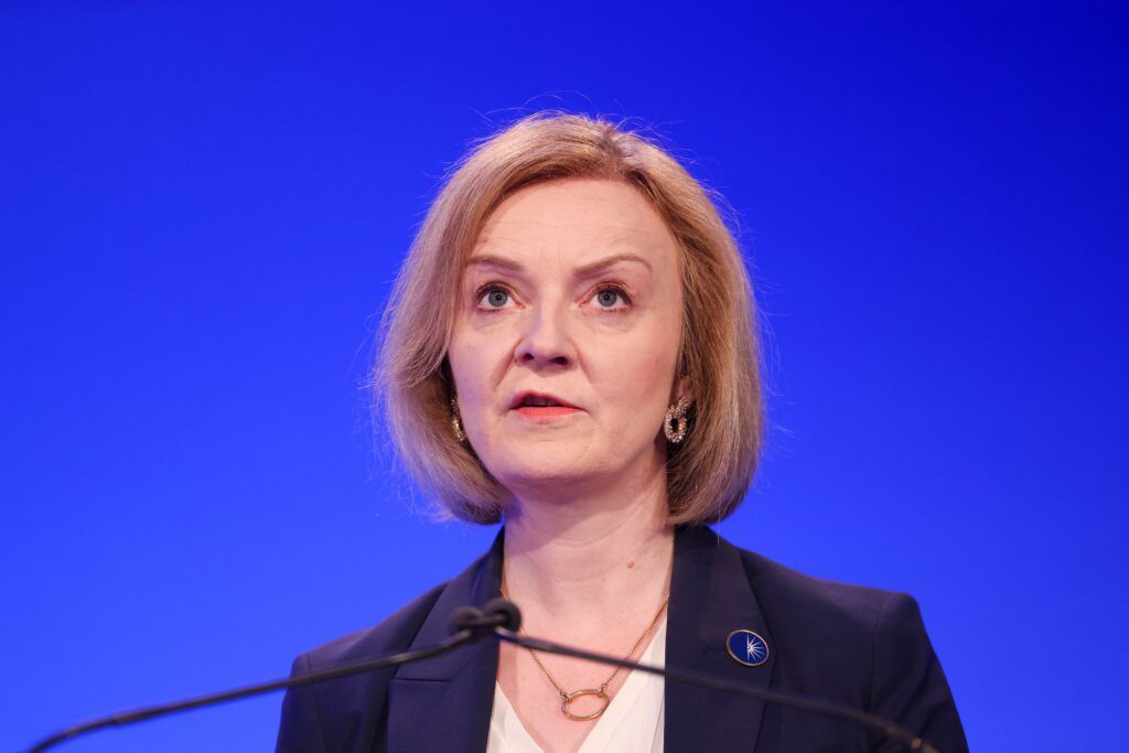 Liz Truss at a podium speaking, the background is blue