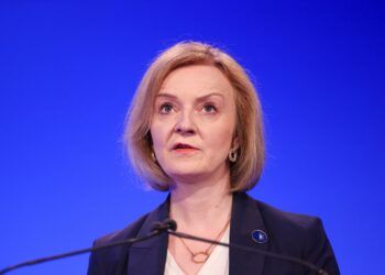 Liz Truss at a podium speaking, the background is blue