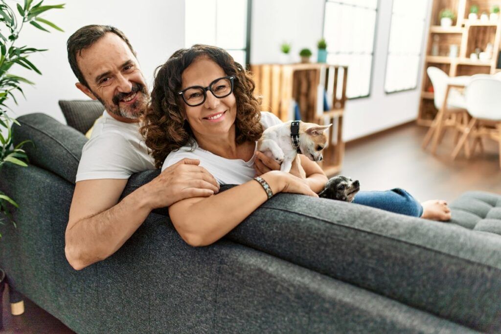 couple leaning over back of sofa, woman holding small dog.