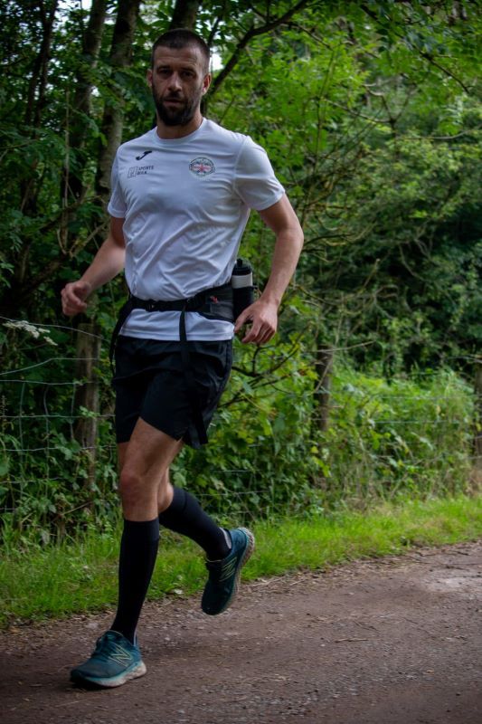 Darren Blanks running down a woodland path. He is wearing a white t-shirt, running belt and black shorts.