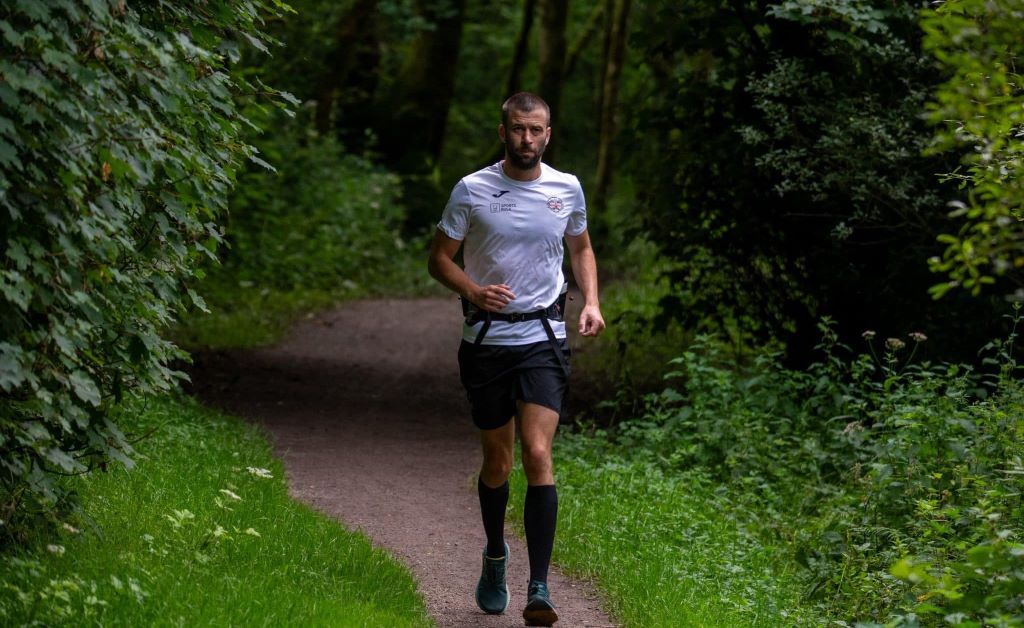 Darren Blanks is pictured running down a woodland path. He is wearing a running belt, a white t-shirt and black shorts.